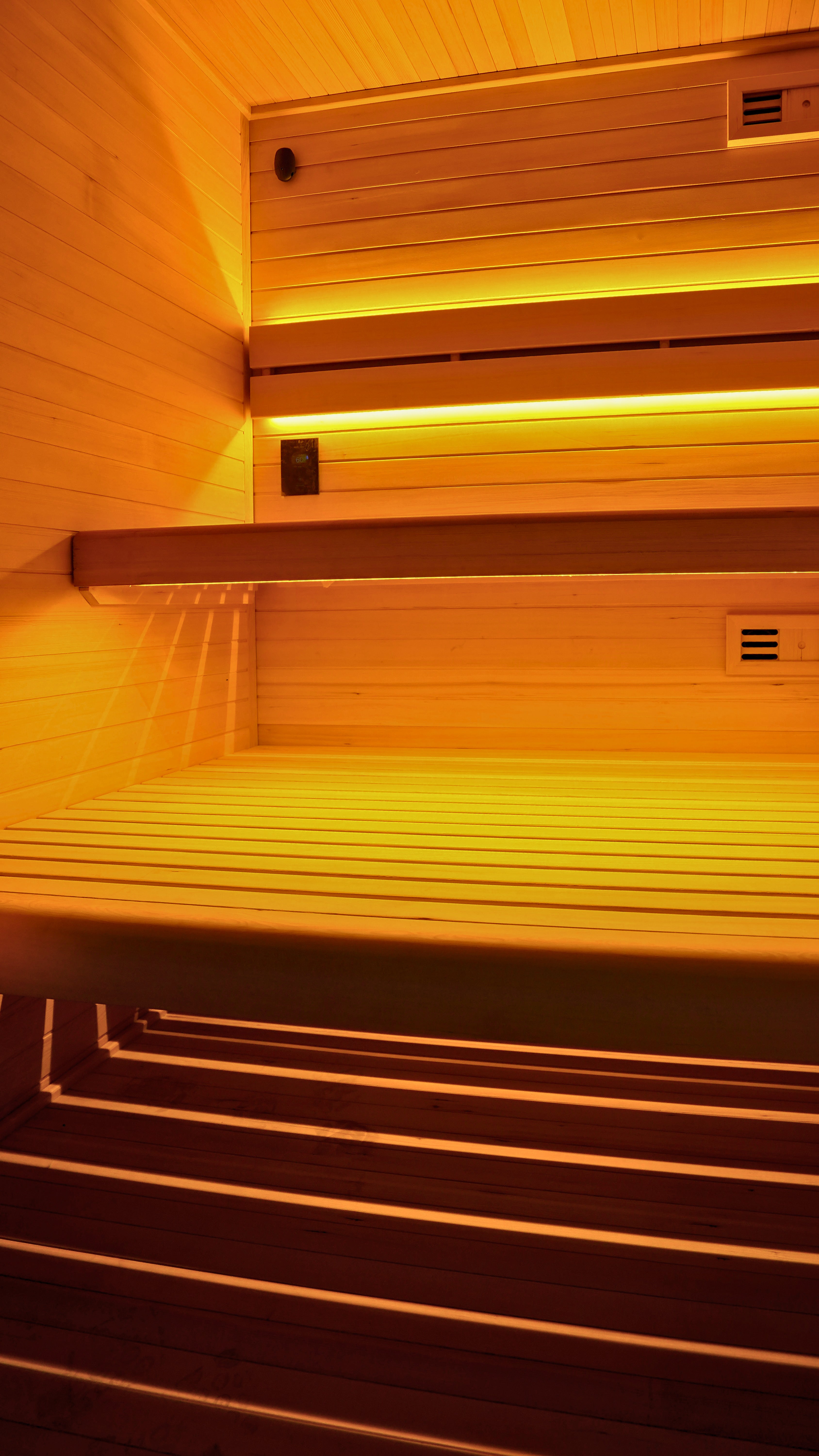 Wooden sauna interior with tiered seating and warm yellow ambient lighting.