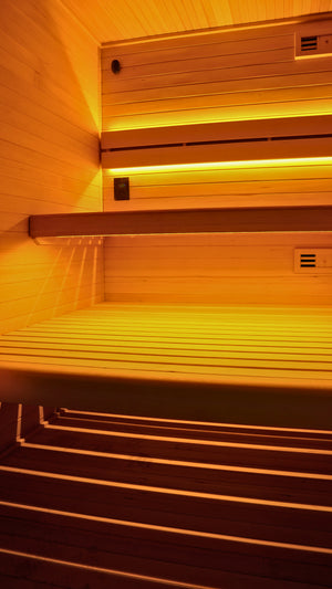 Wooden sauna interior with tiered seating and warm yellow ambient lighting.