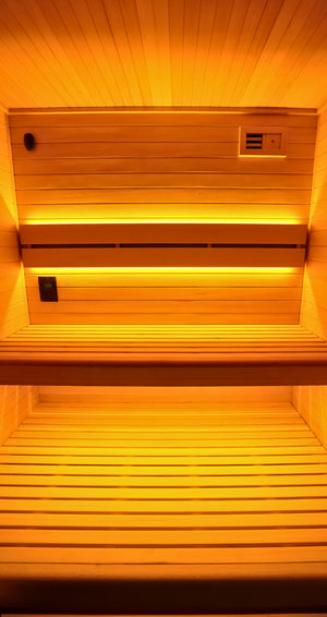 Wooden sauna interior with two tiers of slatted seating, backlit by warm yellow-orange ambient lighting.