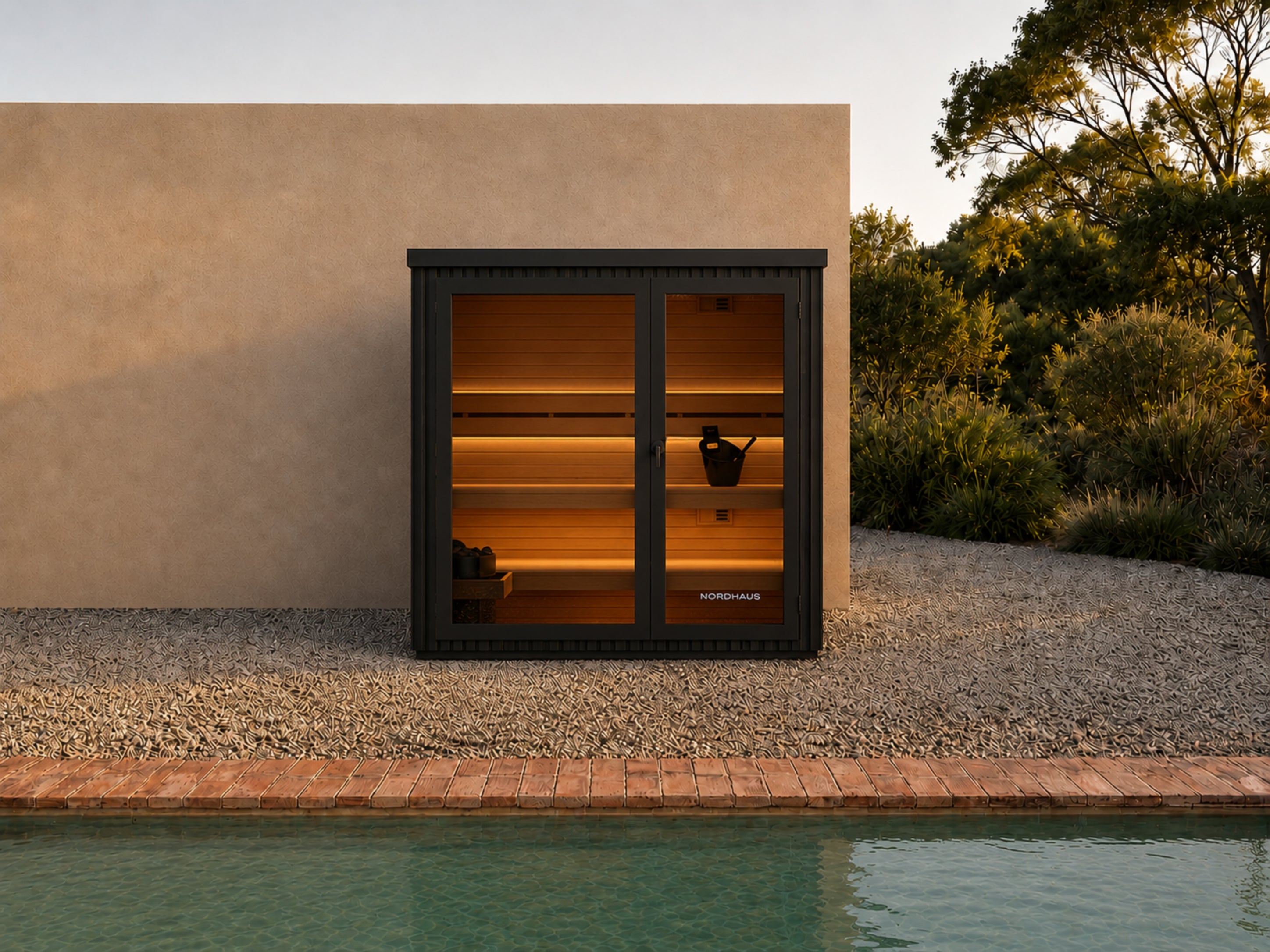 Modern outdoor traditional sauna beside a swimming pool with black aluminium exterior, large glass front window and door, warm LED-lit Canadian Hemlock interior, and minimalist landscaped backyard setting at sunset.