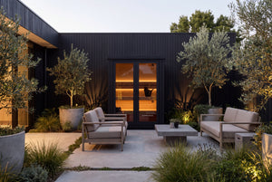 Black Nordhaus outdoor traditional sauna with a warm timber interior, set within a landscaped modern courtyard with outdoor seating and olive trees.