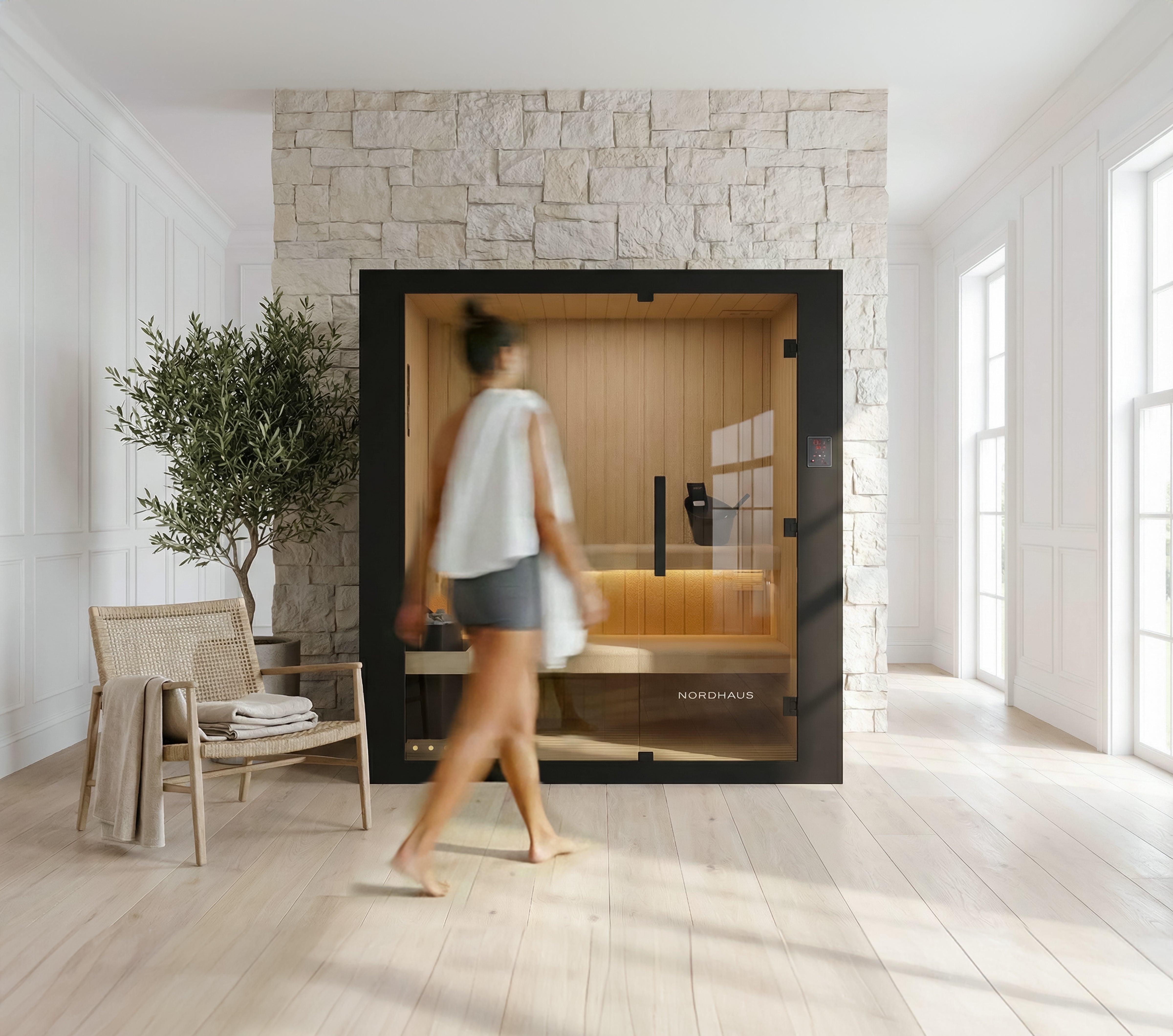 Woman walking towards a modern sauna in a stylish room with stone wall and wooden floor.