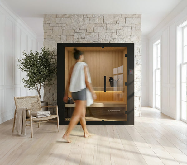Woman walking towards a modern sauna in a stylish room with stone wall and wooden floor.